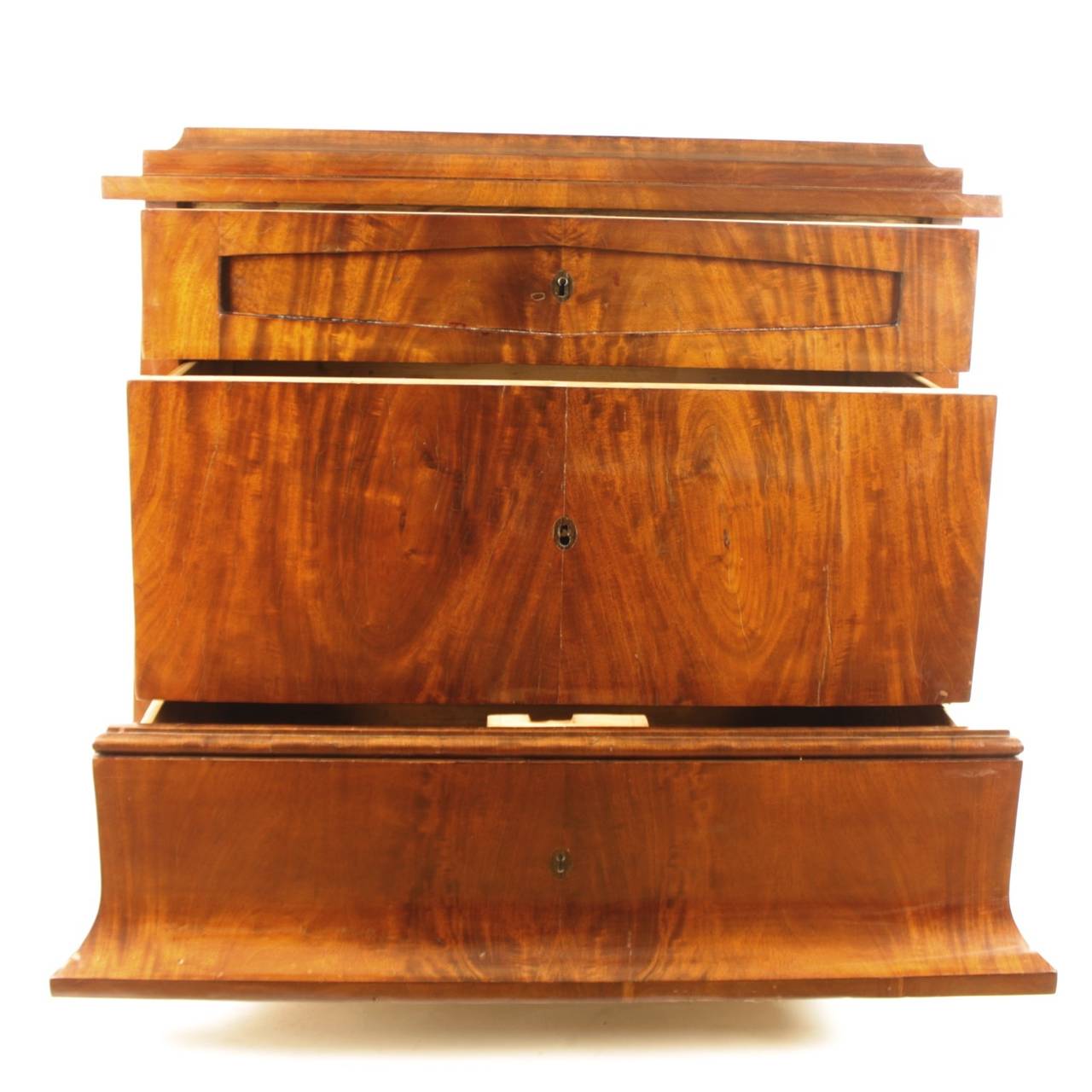 Biedermeier commode with tapering breakfront corpus and stepped pediment, with three long drawers on block feet. The whole veneered with mahogany on pine in book-match pattern - the wood with its grain configuration being the most important motif of