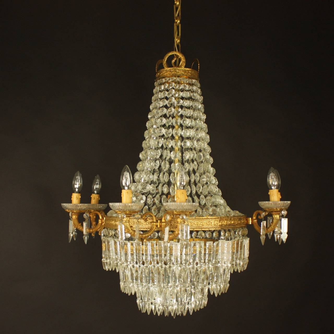 The circular top corona hang with facetted drops, with a central tier decorated with foliate, fitted with eight scrolled candle branches with suspended prism drops, the lower body consisting of three rows of prism drops with one interior light.