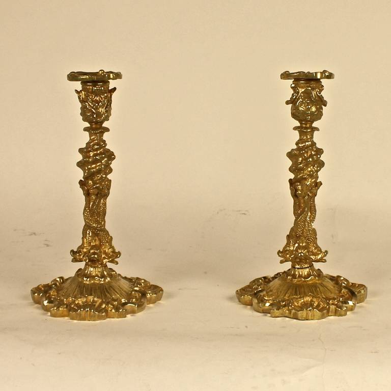 A pair of 18th century ormolu candlesticks representing a maritime theme with shells and rocks on the nozzle, three entwined dolphins forming the shaft above a base depicting water surrounded by shells. Finely chased bronze work with gilding of