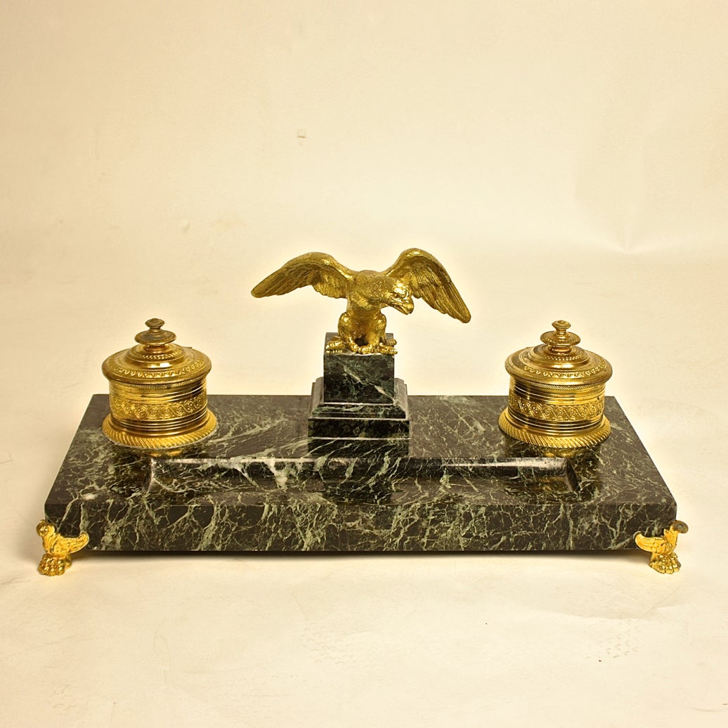 A fine marble and gilt-bronze Encrier set consisting of a letter rack and double inkwell set of richly-veined Verde Antico marble. The concave cutout for writing instruments flanked by two inkwells with porcelain insets, surmounted by a  eagle