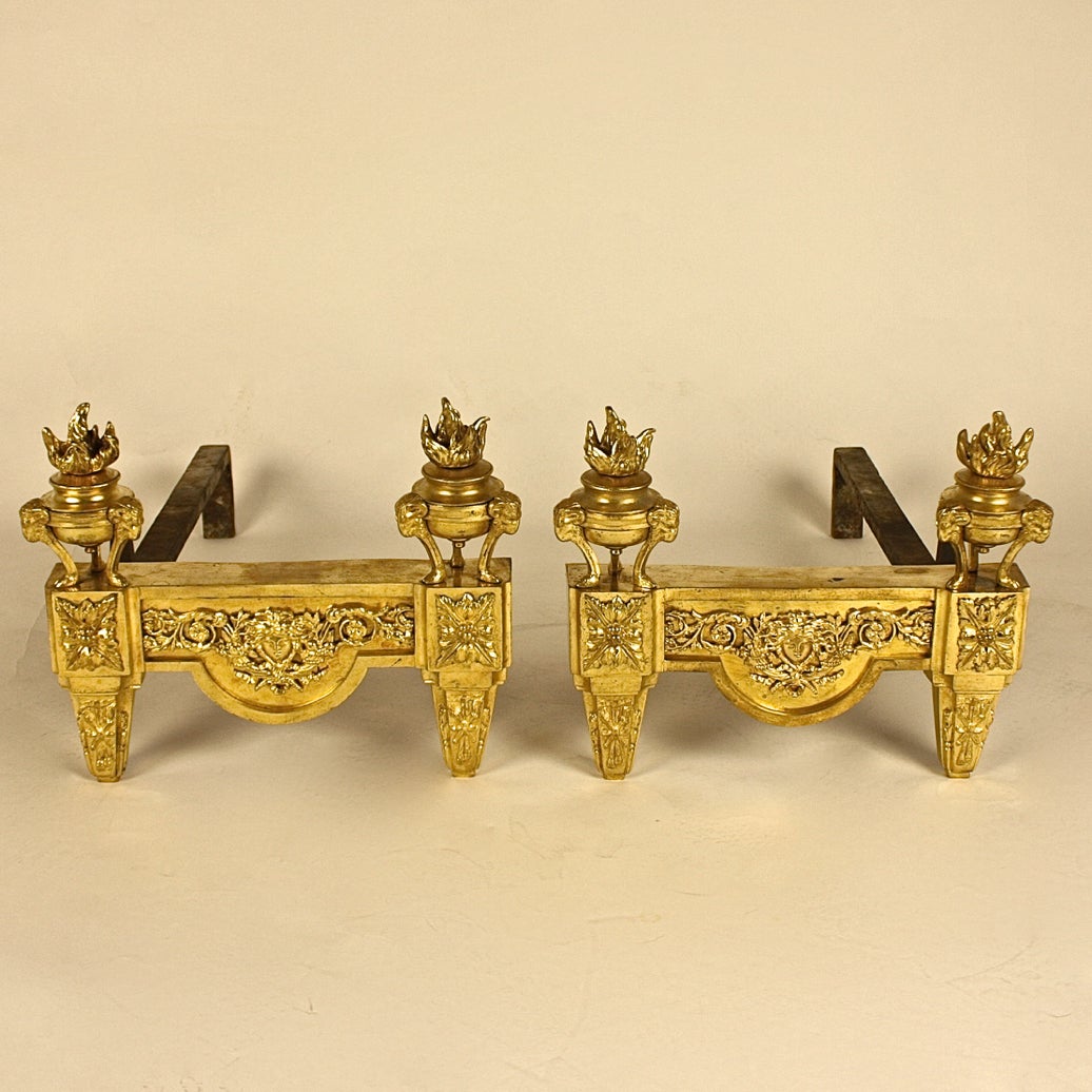 A pair of Louis XVI style ormolu chenets, cast by Bouhon Fre`res, Paris, late 19th century. Each modelled with two flaming athe´niennes supported by hoof monopodiae surmounted by rams' masks, the shaped plinth mounted to the centre with the mask of