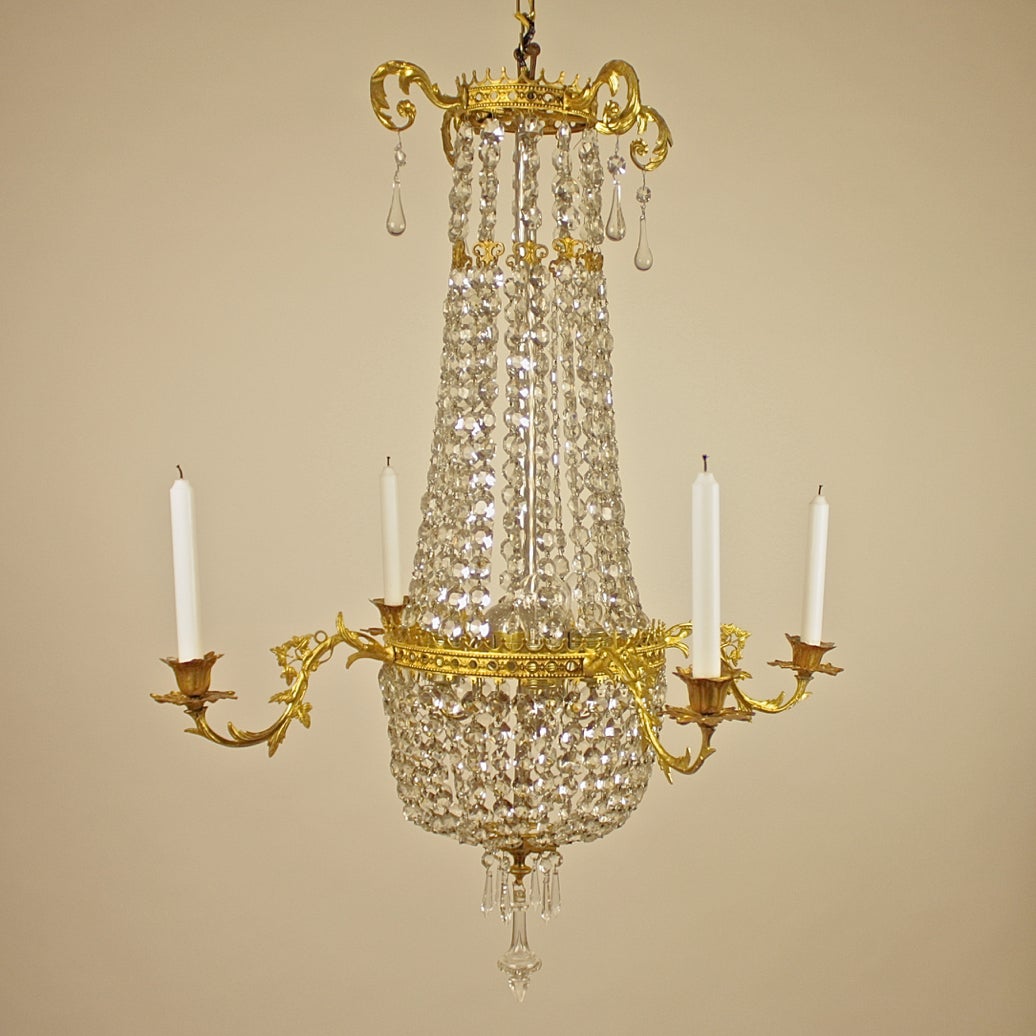 An elegant ormolu cut-crystal chandelier, the pierced and crown-shaped corona hang with chains of crystal drops, the chains fork off aided by an volute-shaped piece, with the central crown shaped ring issuing four candle arms, the whole hang with