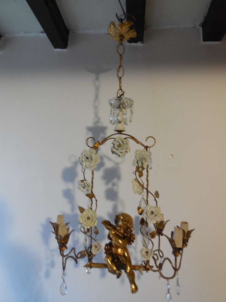 Housing 6 lights!  Gold tole swing with huge white porcelain roses.  Crystal bobeche on top.  Darling big gold cherub in center.   Adding 10” of original chain and canopy. Piedmont region. Need to be rewired for U.S. safety standards.