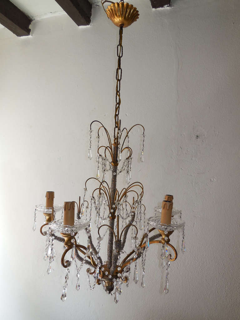 Housing five lights, sitting in vintage crystal bobeches, dripping with vintage crystal prisms. Five arms and center complete with micro beading. Swags of crystal beads and adorning many florets and crystal prisms. Gilt wood under bobeches and as