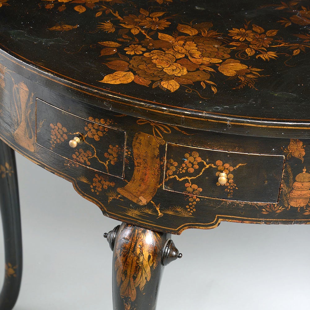 An early 20th century side table in the Queen Anne taste, the demi-lune top above a frieze with two short drawers and two dummy drawers, all raised upon three cabriole legs and decorated throughout with gilt chinoiseries upon a black ground.