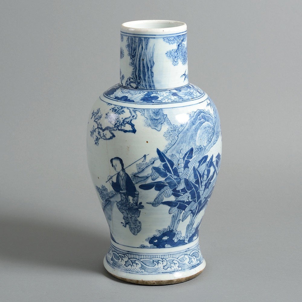 A late 19th century blue and white porcelain vase, of baluster form, the body decorated with figures seated at a table within a fantasy woodland landscape. 

Late Qing Dynasty 

(hair line crack to body - see images)