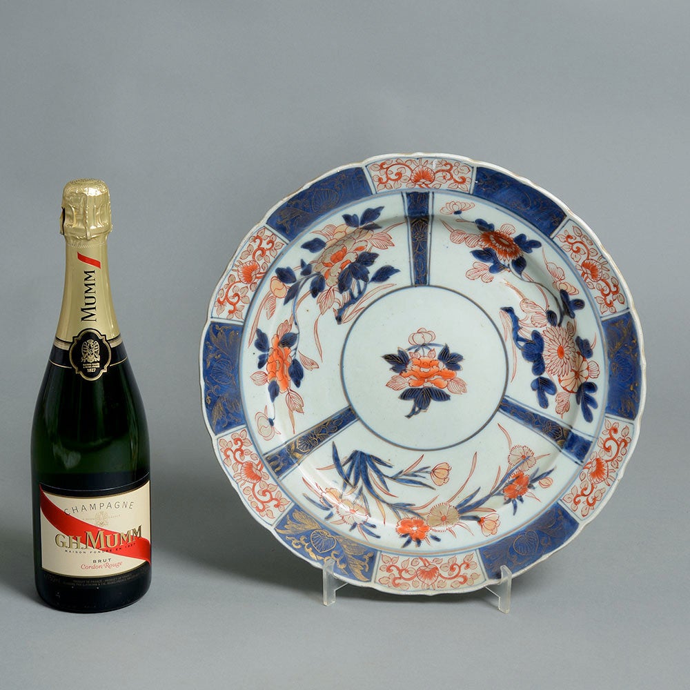 An early 18th century Imari charger, the upper side decorated with radiating panels of floral decoration in red and blue glazes upon a white ground. 

Restored. 

Imari is the name given to porcelain made in the Japanese town of Arita. From the