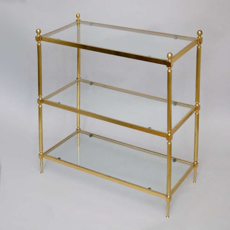 A mid-20th century 3-tire brass etagere, the glass shelves held in a rectangular frame, the fluted support surmounted by turned ball finials.