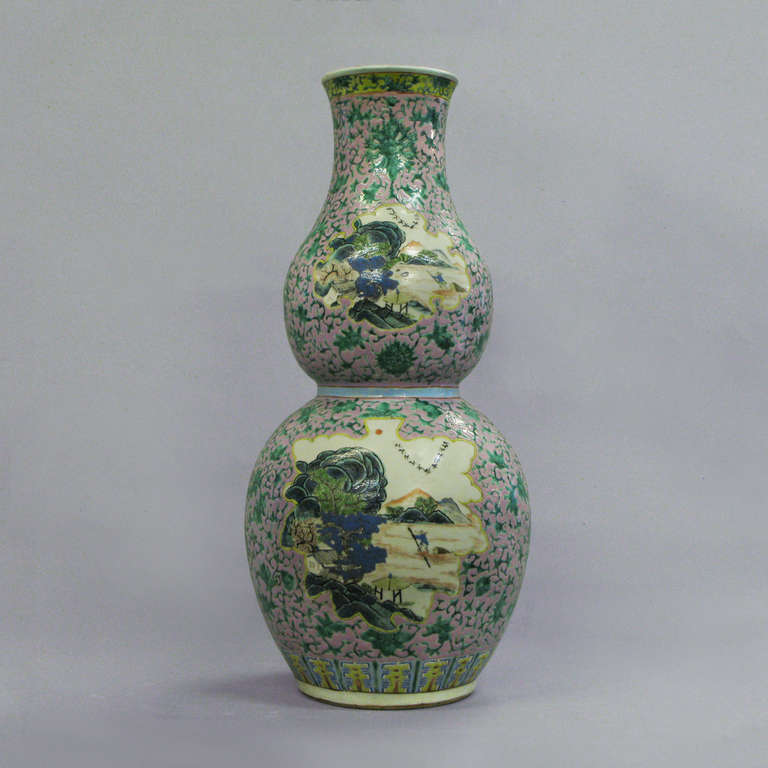 A double gourd shaped porcelain vase of large scale, the pink ground set with leaf form cartouches depicting imaginary landscapes.