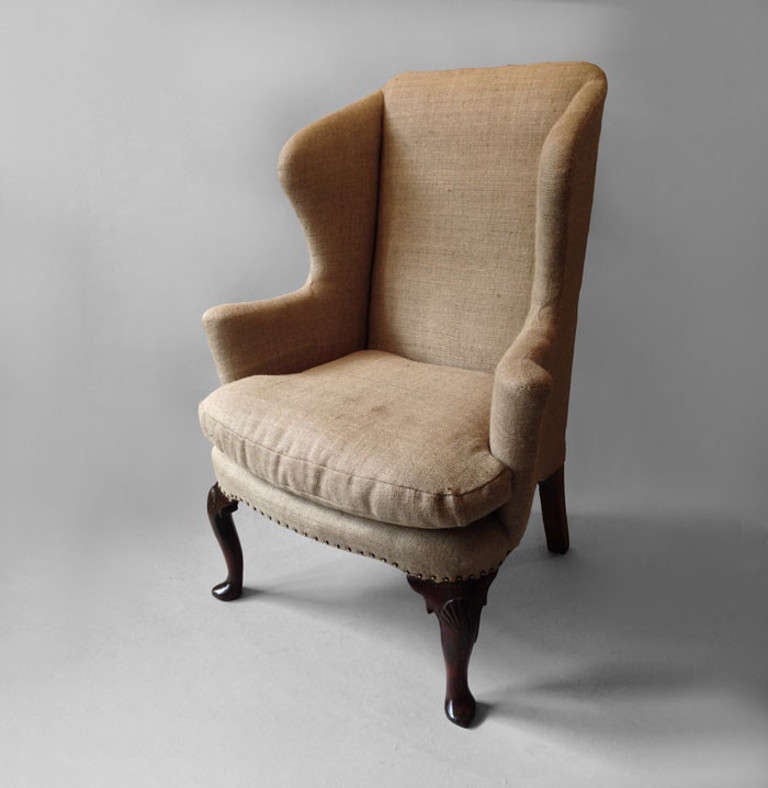 An early 18th century wing armchair the shaped frame with scrolling arm rests raised on carved walnut cabriole legs with scollop shell decoration and pointed pad feet.