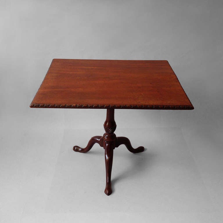 A George III mahogany tripod table, the rectangular top with ribbon and flower carved border and set upon a turned stem with birdcage action, supported on generously carved tripod feet.