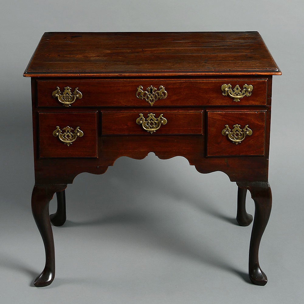A mid-18th century George II Period mahogany low boy, the overhanging top above a configuration of four drawers, with pierced brass handles, above an arched front, set cabriole legs with outward pointing pad feet.