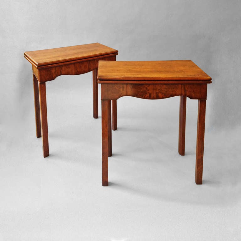 A pair of mid-18th century small scale mahogany card tables, the folding tops opening to reveal baize playing surfaces, the fronts with shaped apron friezes, the sides usually tapering to a veneered hinged back, all raised on for chamfered square