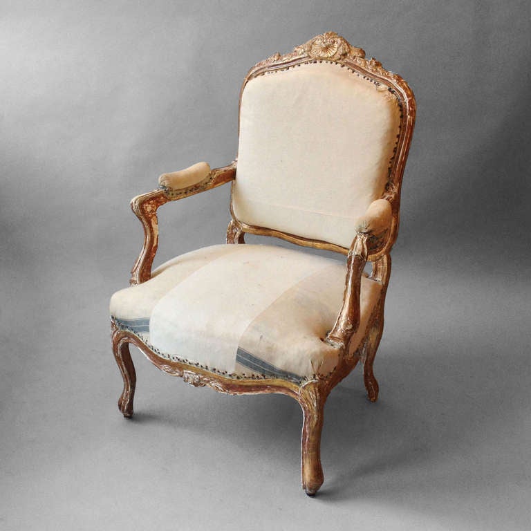 A late 19th Century Carved, gilded armchair or fauteuil in the rococo taste, the upholstered. cartouche back with scrolling upholstered arm rests above a shaped seat frame set upon cabriole legs.