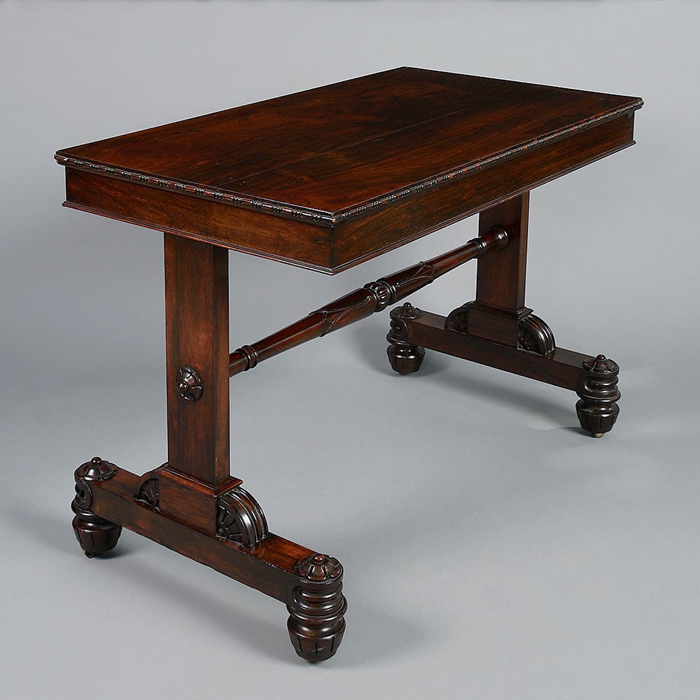 A Late Regency Period rosewood writing table, the rectangular top with finely figured veneers and beading to the rim, set upon two upright supports joined by a turned stretcher with carved decoration, the whole terminating in richly carved bun feet