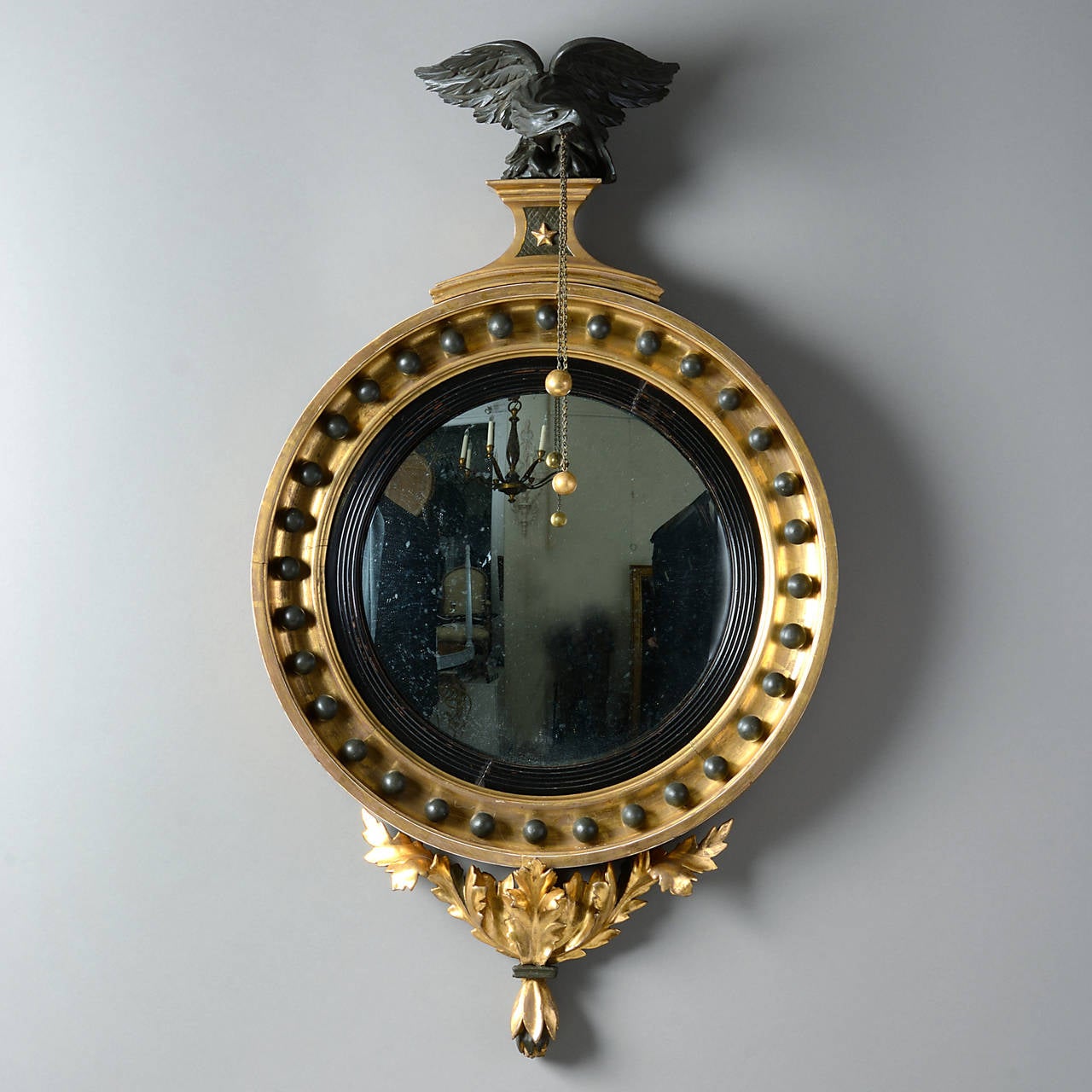 A fine regency Period convex mirror, the circular plate set within a reeded slip, the giltwood frame encrusted with ebonised balls and surmounted with an ebonised eagle clutching balls and chains from its beak, the whole terminating in carved