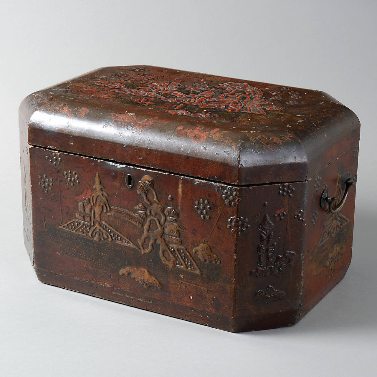 An early 19th century Chinese Export lacquer casket of rectangular form, profusely decorated with pagodas, flowers, birds and trees in a mountainous landscape having chamfered corners and the original brass carrying handles.