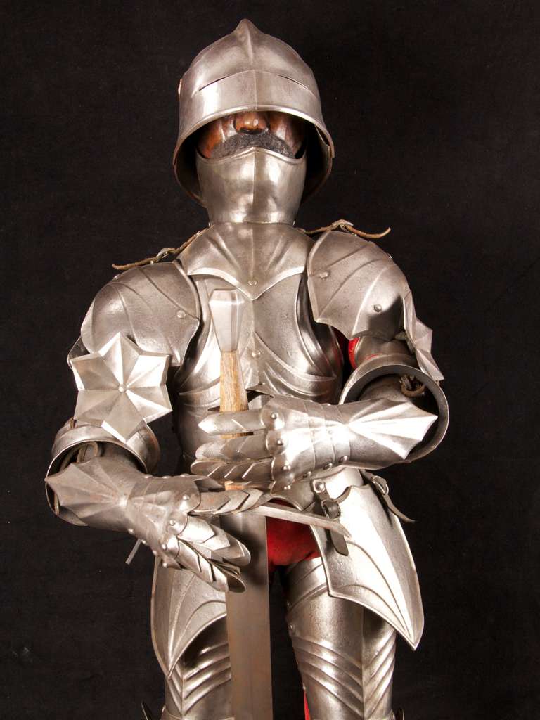 A late 19th Century model suit of South German, late Gothic armour, in the style of circa 1480-1500. 36” high, mounted on a square wooden plinth complete with sword. The hinged sallet (helmet) with viewing slit, it has a carved wood human head