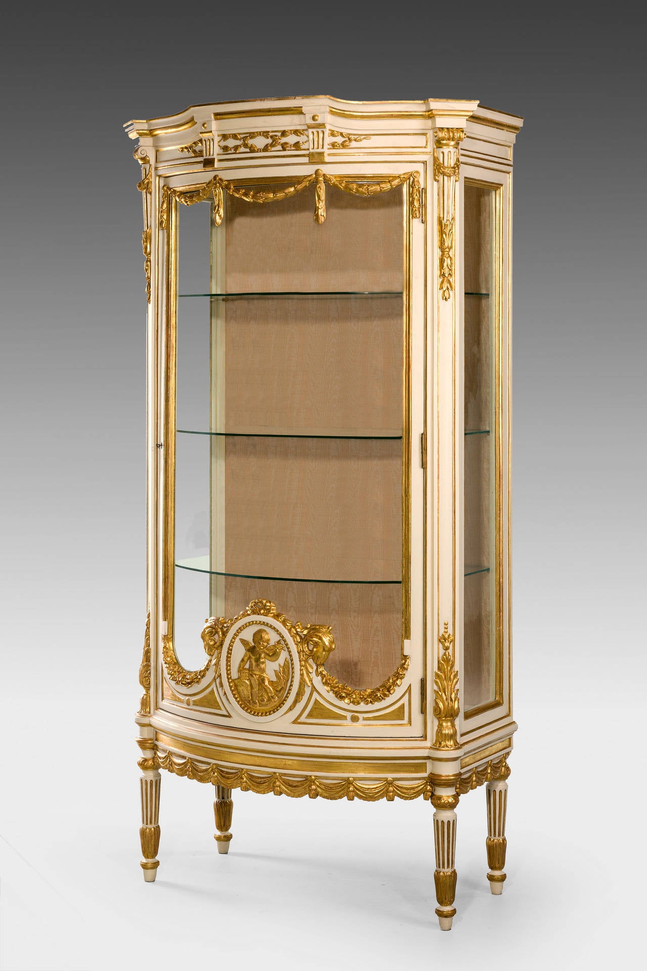 An exceptionally fine 19th Century 'Belle Epoque' China cabinet, soft ivory ground, the finest gilding with 24kt gold leaf, the central cartouche incorporating a Putto, the top with finely carved garlands and leaves. 

A putto (plural putti, /ˈpʊti/