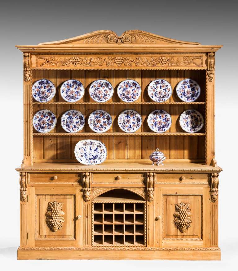 An unusual pine dresser and rack of very substantial construction, the centre section incorporating wine shelves, the door fronts and borders with very well executed carved detail, the upper section with rope cane fruit and vines.

This was