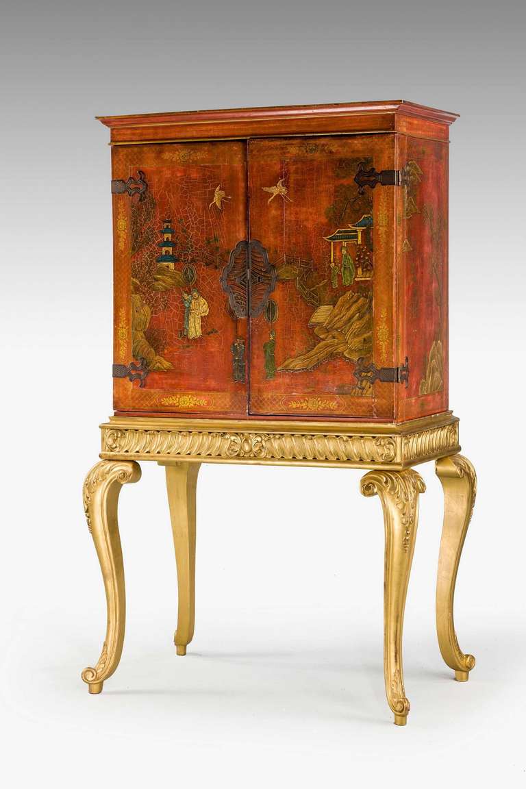 A chinoiserie red lacquered Cabinet on gilt wood stand, the doors finely lacquered with oriental scenes, the interior doors with 17th century marquetry designs, the whole on gilt wood cabriole supports.