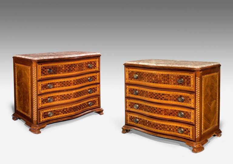 A complex pair of serpentine Iberian commodes, the facade with interwoven panels of quarter cross grain timbers including king wood, boxwood and satinwood on ogee supports, all under inset marble tops, second quarter of the 19th century.