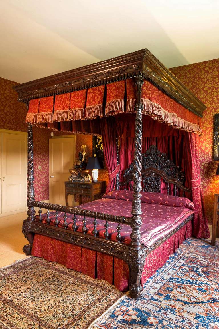 A 19th century Indian four-poster bed, an exceptional black wood bed, all the carved elements of quite outstanding quality, the open work pierced supports under a canopy with scroll work and pleats, the headboard with an insignia of the family the