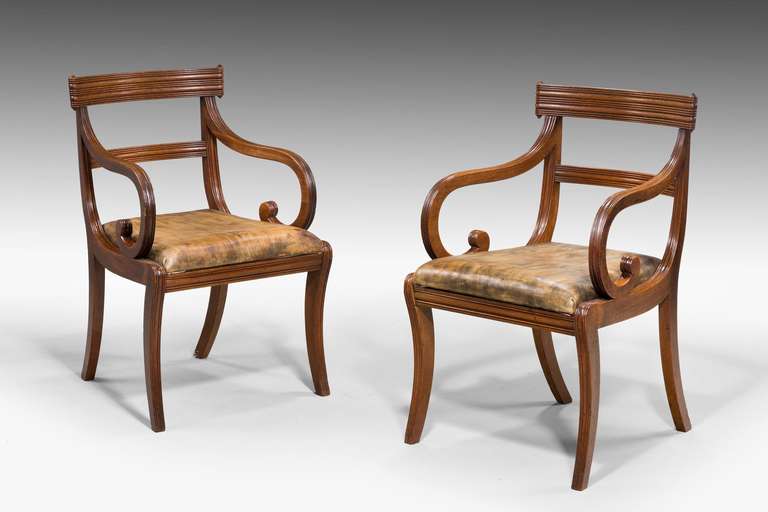 A good pair of Regency period mahogany sabre leg elbow chairs, the top rail with a wraparound carved design, scroll arms over well defined sabre supports.

