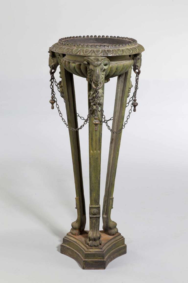 A patinated cast iron floor-standing Athenienne, the masks joined by chains, the supports terminating in elaborate paw feet over a triform stepped base.