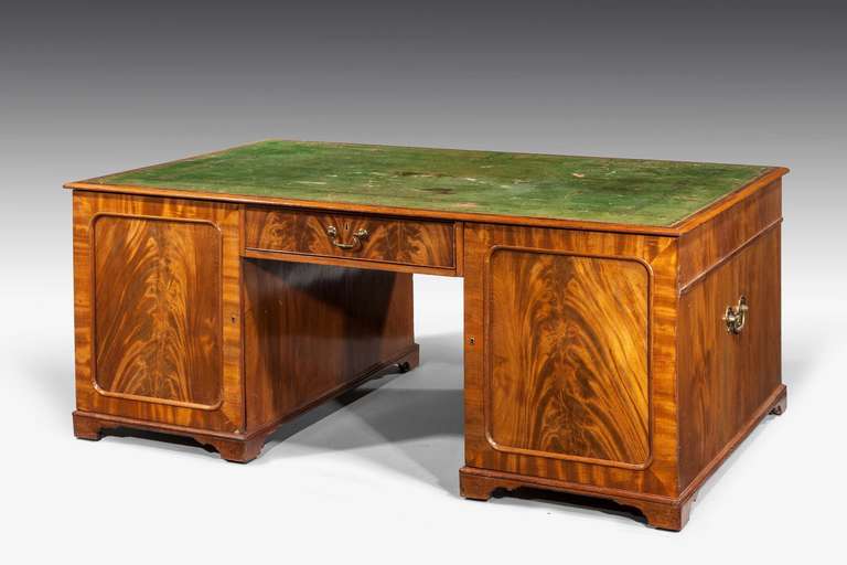 A very finely figured late Regency period mahogany partners desk with an old, somewhat tired, green inset leather top, a very good golden color and patina, swan necked handles, the reverse with matched inset cupboard doors and single drawer.