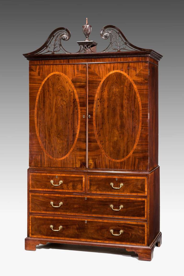 A fine 18th century George III period mahogany gentleman's press with finely carved open fretwork swan neck pediment above a dentil moulding. The oval panels to the doors and drawer fronts with satinwood crossbanding.