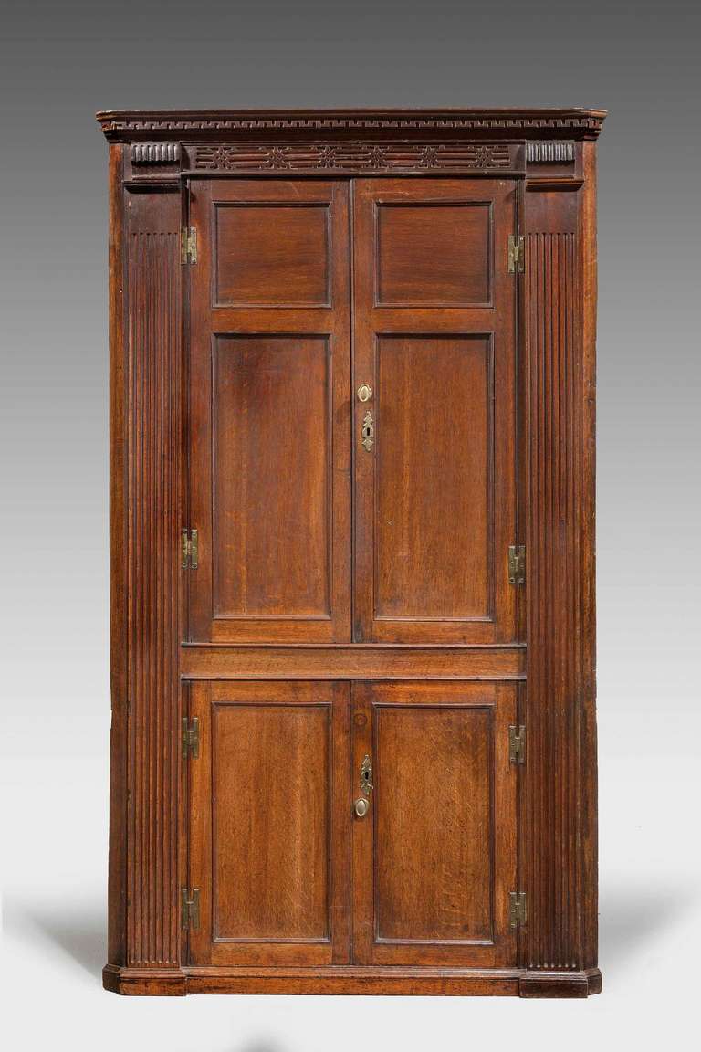 A good George III period double oak corner cupboard, the uprights with incised reeded decoration, the doors with a finely molded edge, the top with sharply carved dentil corners, all on a plinth base. Four shelves to the upper section and two