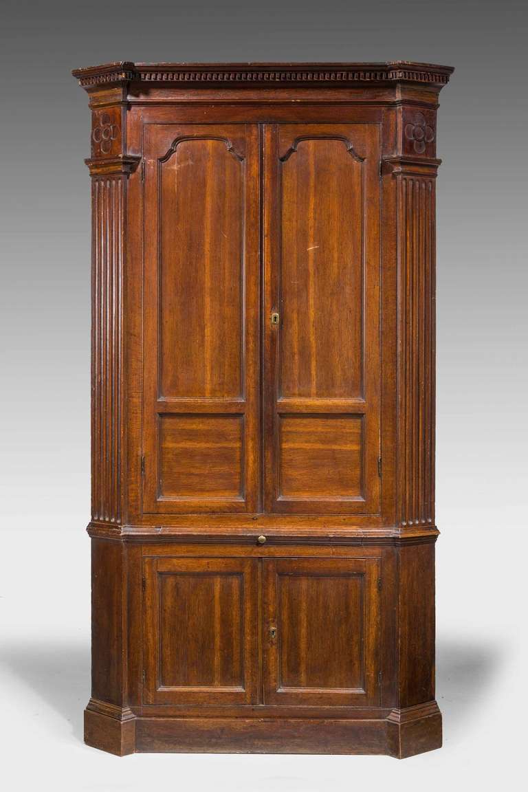 A George III oak double corner cupboard, the top border with blind fret carving and reeded billesters, the interior shell shaped with four shelves.

