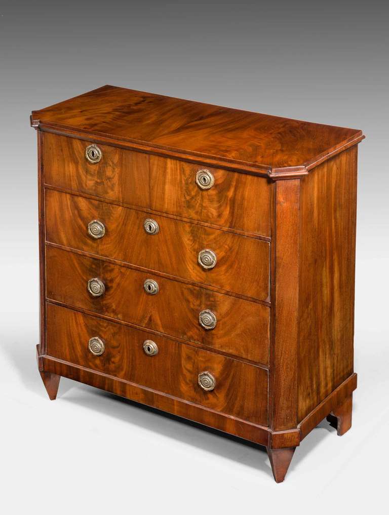 An elegant and finely figured Early 19th Century mahogany Chest of Drawers of very small proportions, oak lined, the timbers flowing through the facade including the sides, canted corners standing on original tapering supports, finely chiselled and