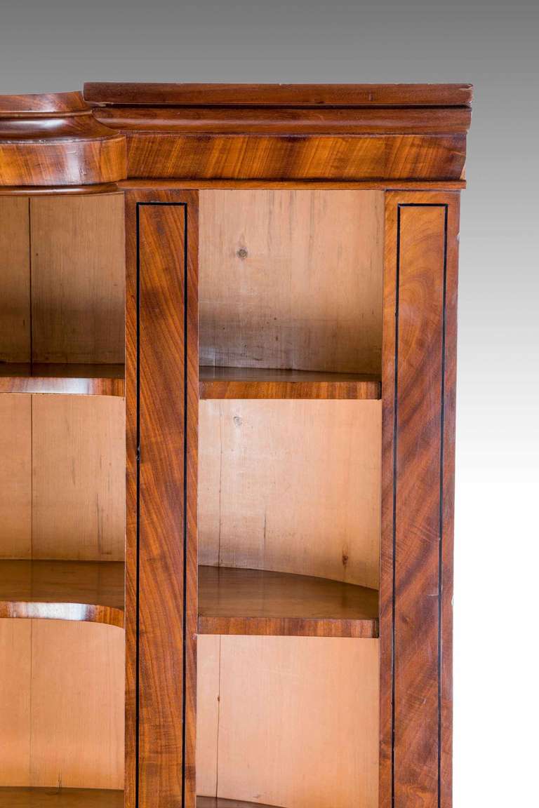 Regency period mahogany demilune and break front open bookcase, unfinished to the reverse, very well figured veneers with ebony line, cross banded front edge shelves.


