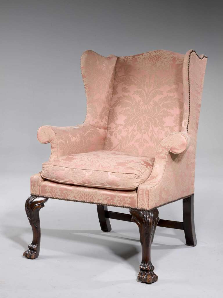 A good mahogany framed George II period wing chair of small proportions on well carved cabriole supports, the knees with stylized foliage carving terminating in paw feet.