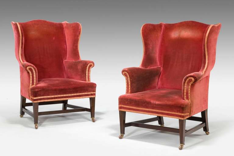 An attractive pair of shapely mahogany wing chairs of Chippendale design with square supports and cross stretchers.

