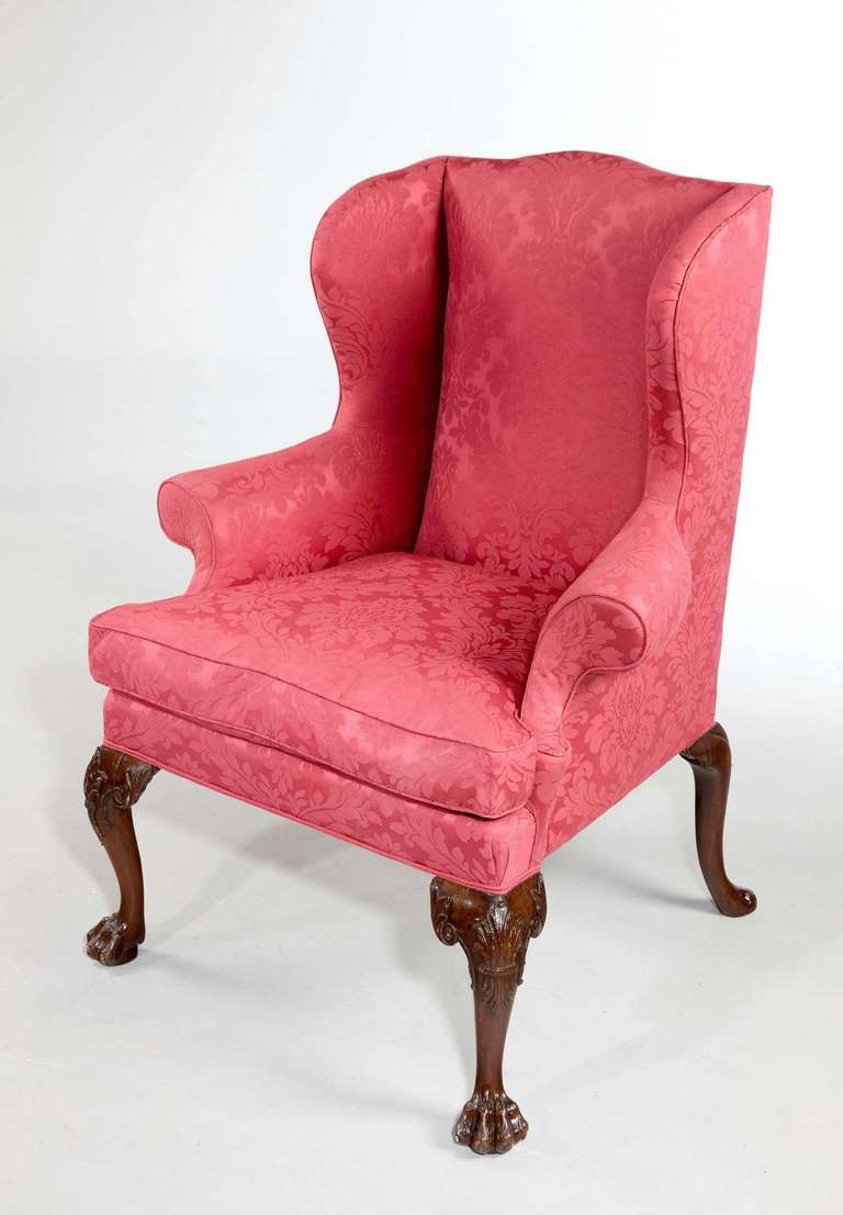 A fine George II period mahogany framed wing chair. Reference for a similar pair of carved mahogany library armchairs, with almost identical carving, but with trailing bell flowers and pad feet which may have formed part of a set of armchairs and