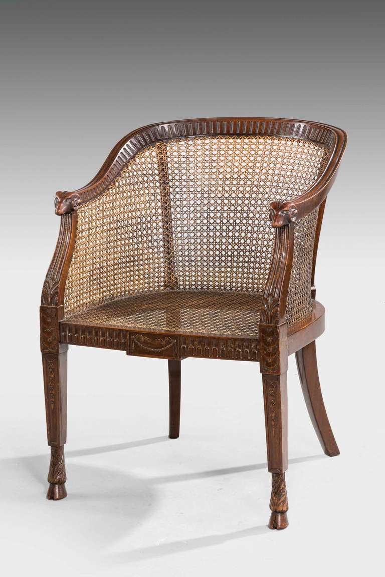 Late 19th century well carved bergere armchair, the arms terminating in rams heads, supported on rams feet. Archaic reeding and bow fronted seat rail. 

Provenance:
Appearing first in Paris during the Régence (1715–23), the form reaches its full