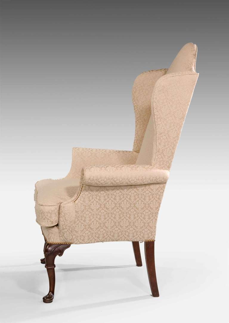 An attractive George I design walnut framed wing chair, well carved decoration to the front supports now covered in fine champagne colored fabric.

