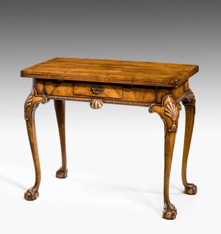 An exceptionally fine quality walnut games table of very good design, the top opening in an envelope form, the supports with very well carved shells on cabriole legs terminating in claw and ball feet, a single drawer to the freeze, the top cross
