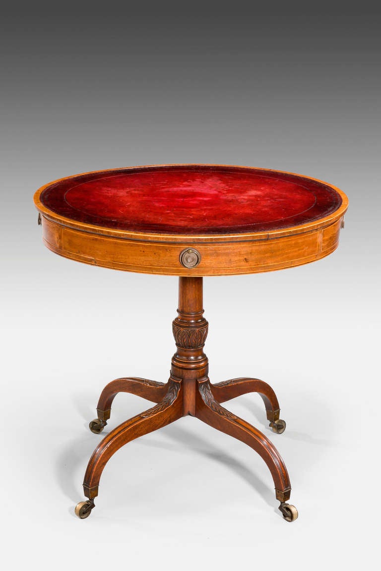 A rare and small George III period mahogany drum table, the oval top with kingwood crossbanding, an old but not original red leather inset top. The turned support over four umbrella legs with finely carved acanthus carving.


   