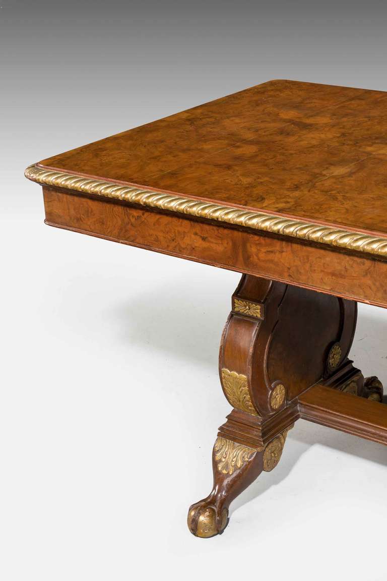 An attractive walnut and parcel-gilt center/library table, the top with eight panels of very fine matching burr timbers, lyre shaped supports joined with a flat stretcher, short cabriole supports terminating in claw feet with softly gilded