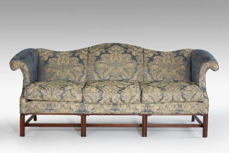 Mahogany framed camel back sofa of Early 20th Century Chippendale design on chamfered square supports the tops with scroll carvings with cross stretchers.