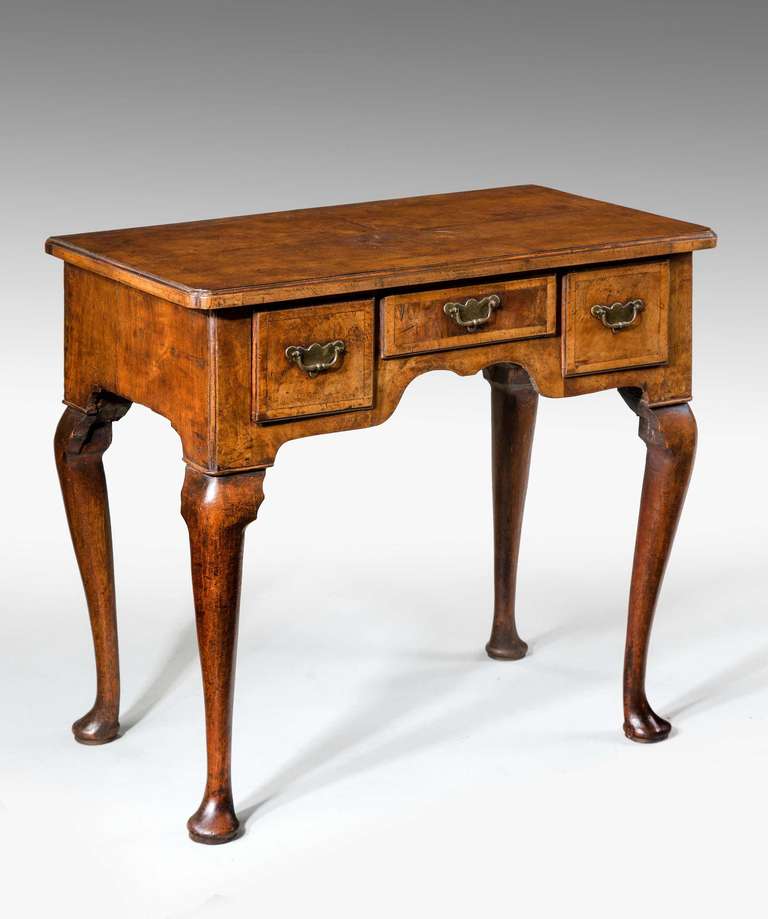 A Queen Anne period walnut lowboy, the quartered top with feathered banding and re-entrant corners, the drawer fronts cross banded with period engraved brass.

