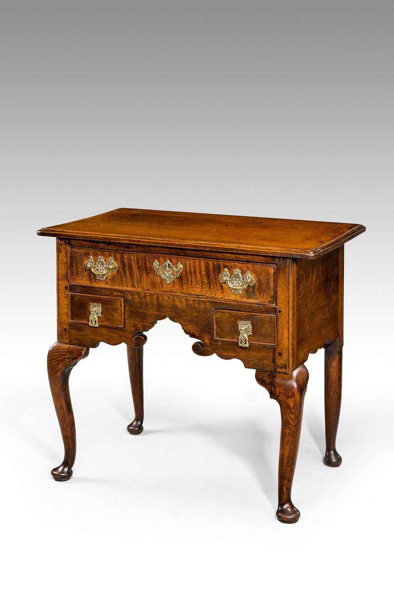 A very well figured George II period oak lowboy, the top with gently rounded corners with a long drawer over two short drawers, a well-shaped apron with quite sturdy cabriole supports terminating on pad feet.

