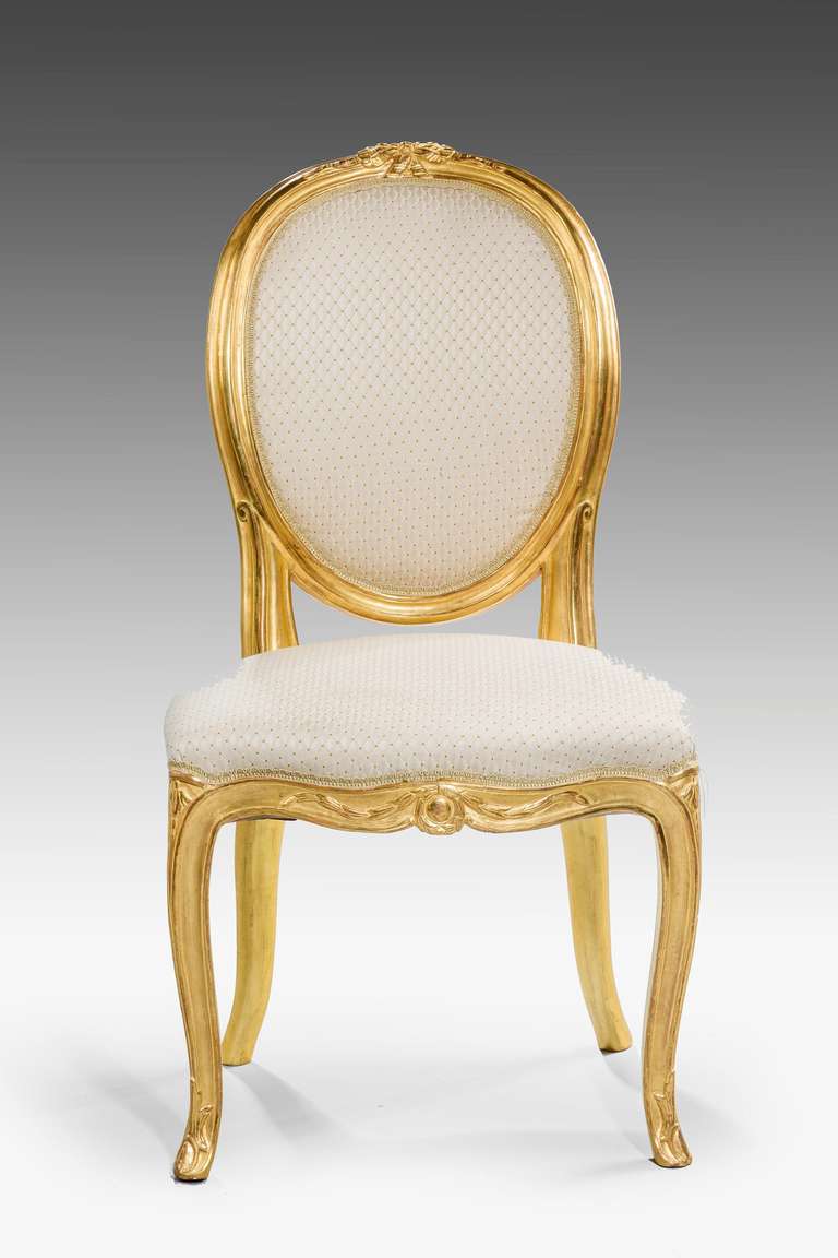A good pair of George III period Gilt-wood Chairs, the oval upholstered backs surmounted by a flower and ribbon emblem, serpentine front rail. ( Second of three pairs )

RR