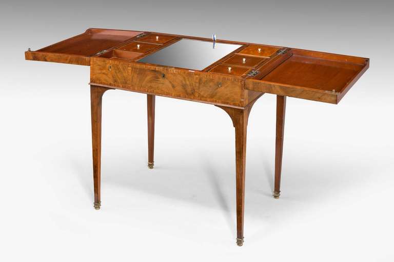 A good George III period mahogany Gentleman's Dressing Table, the envelope opening top over a triple cross banded façade, the interior with a rise and fall mirror together with six compartments, on finely tapering supports ending in gilt bronze shoes
