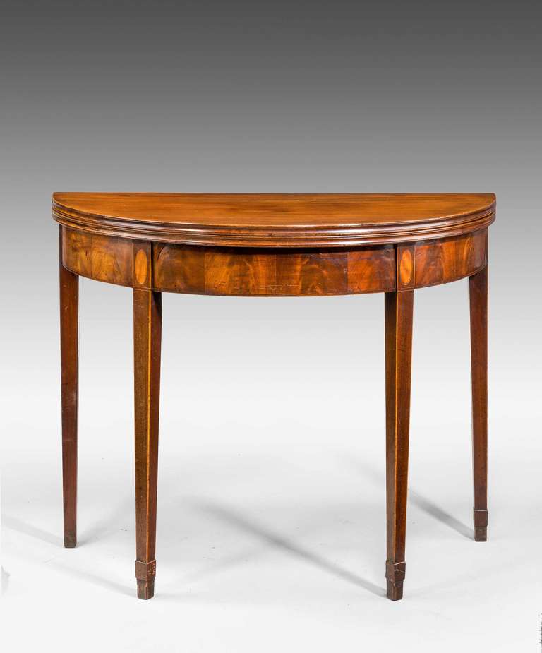 A George III period demilune mahogany tea table, the freeze with unusual veneered panels of flame mahogany, square tapering supports with oval boxwood patera and boxwood edging.

RR.