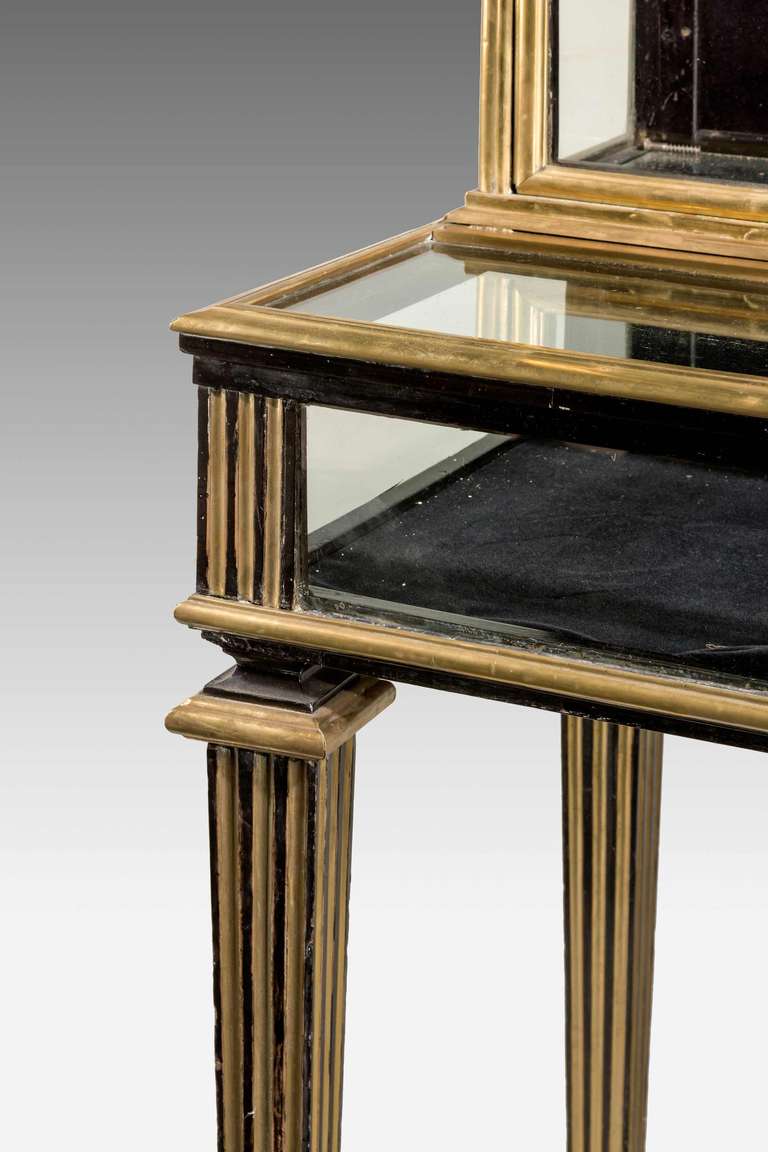 An ebonized mahogany display table or China cabinet, the surfaces with gilded brass mouldings and inset reedings, square tapering supports.

Height to the top of the table = 34 inches
